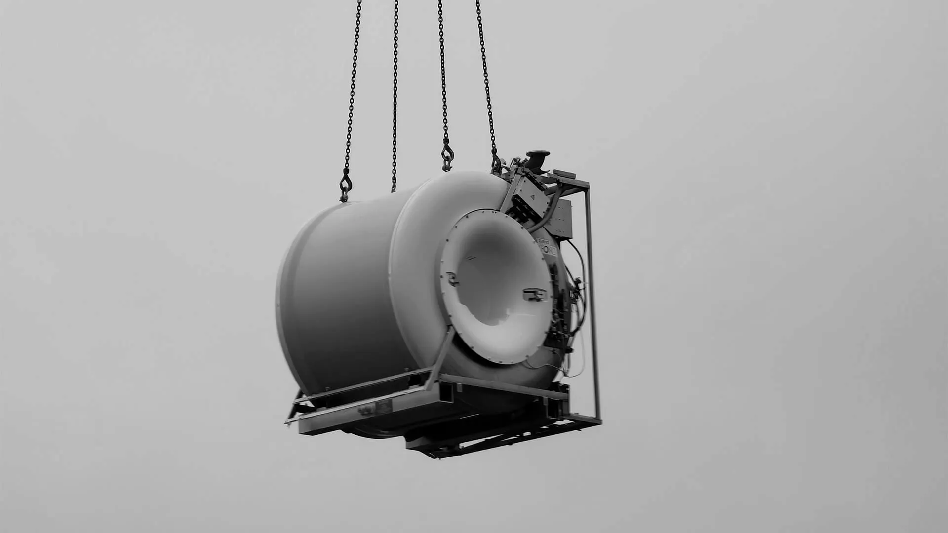 Freigestellter MRT-Magnet schwebt am Kranhaken vor grauem Himmel