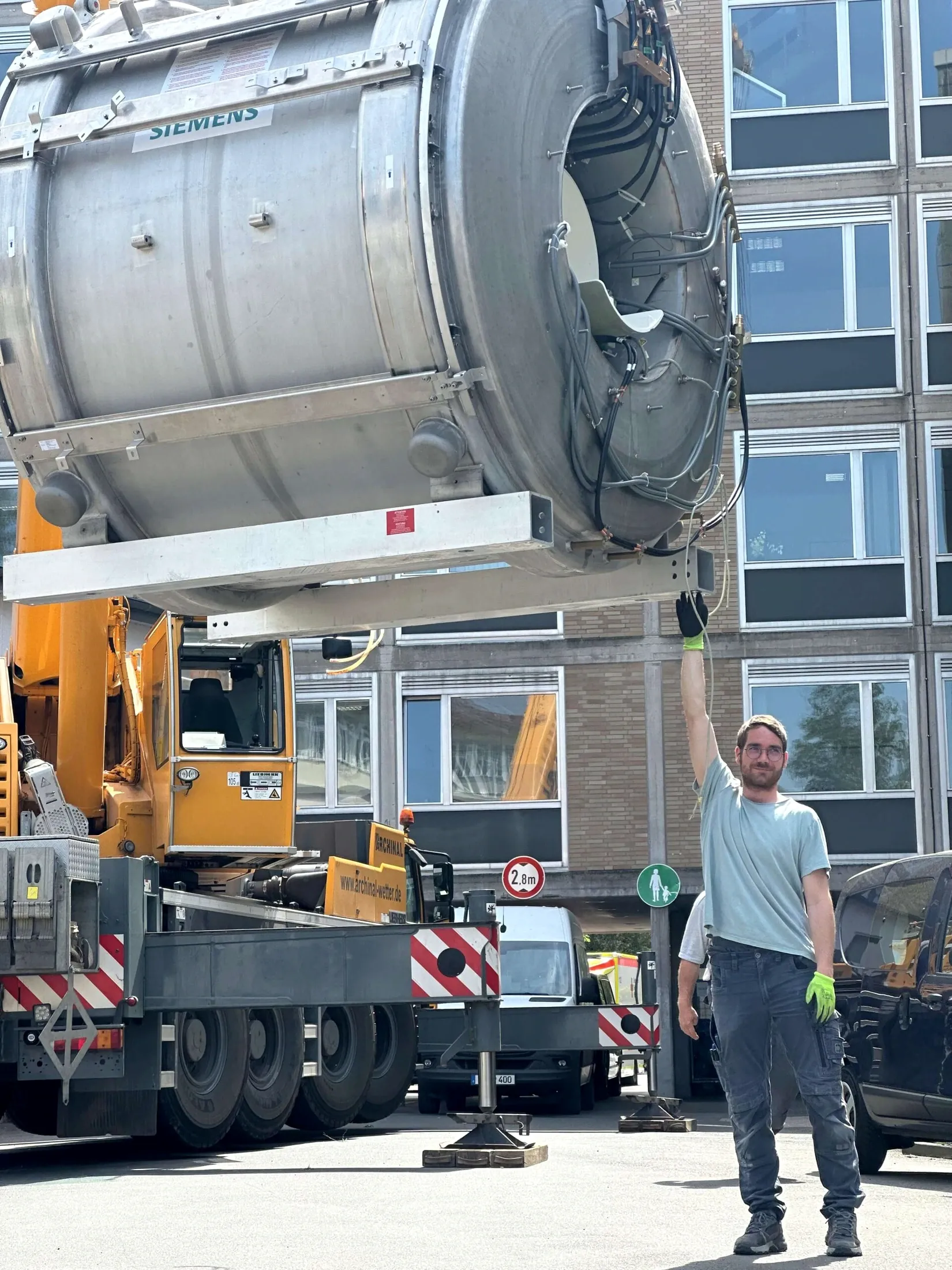 Mitarbeiter gibt am freistehenden Siemens-MRT am Kran ein Handzeichen