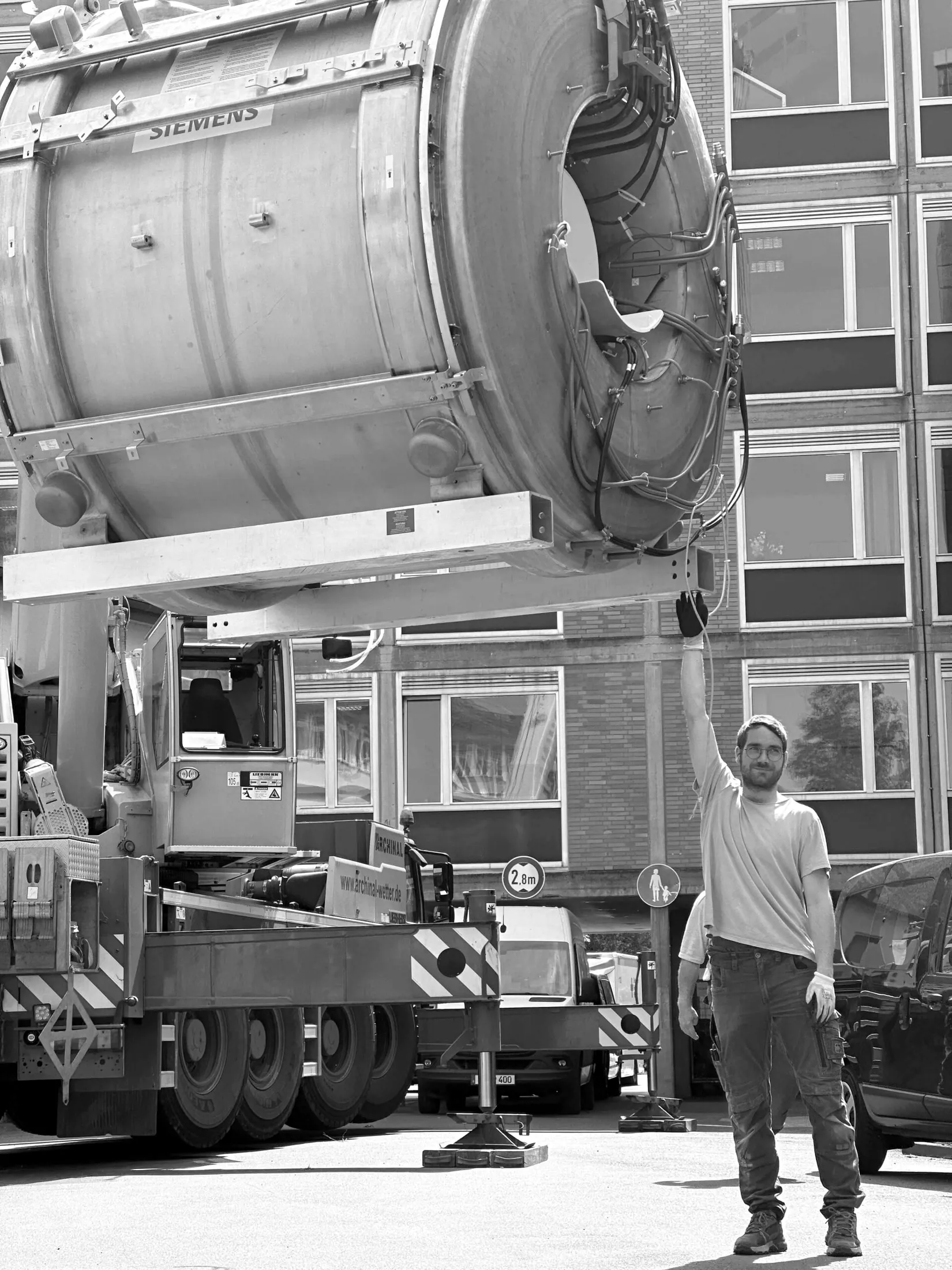 Siemens-MRT am Kran, ein Mitarbeiter gibt das Handzeichen zum Verladen